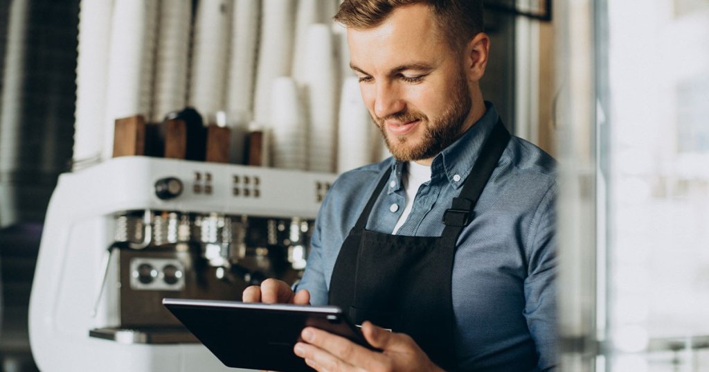 Barista steht mit Tablet vor Kaffeemaschine.