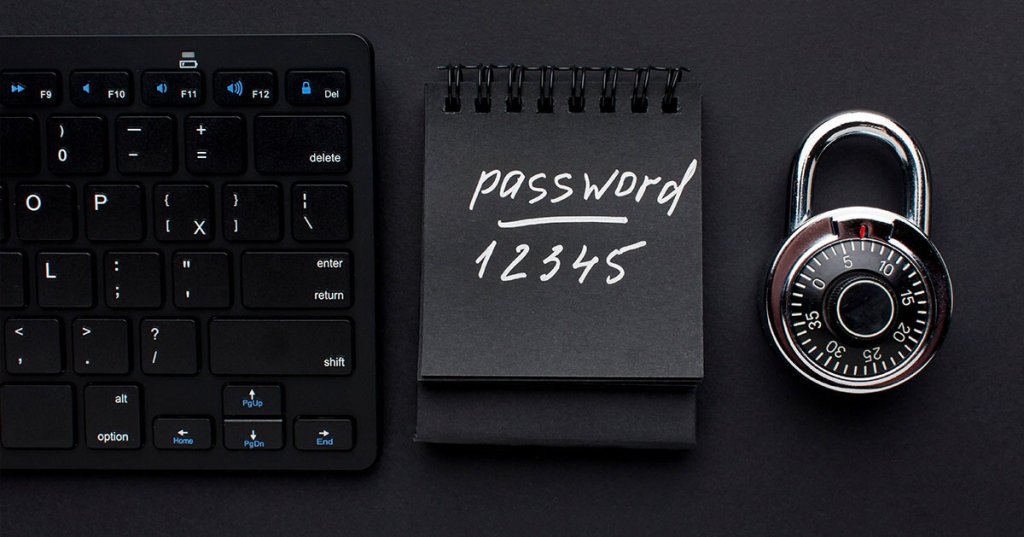 Ein schwarzer Blog mit der Aufschrift "password 12345" liegt auf einem schwarzen Grund. Rechts davon liegt ein schwarzes Zahlenschloss. Links davon ist ein Abschnitt einer schwarzen Tastatur zu sehen.